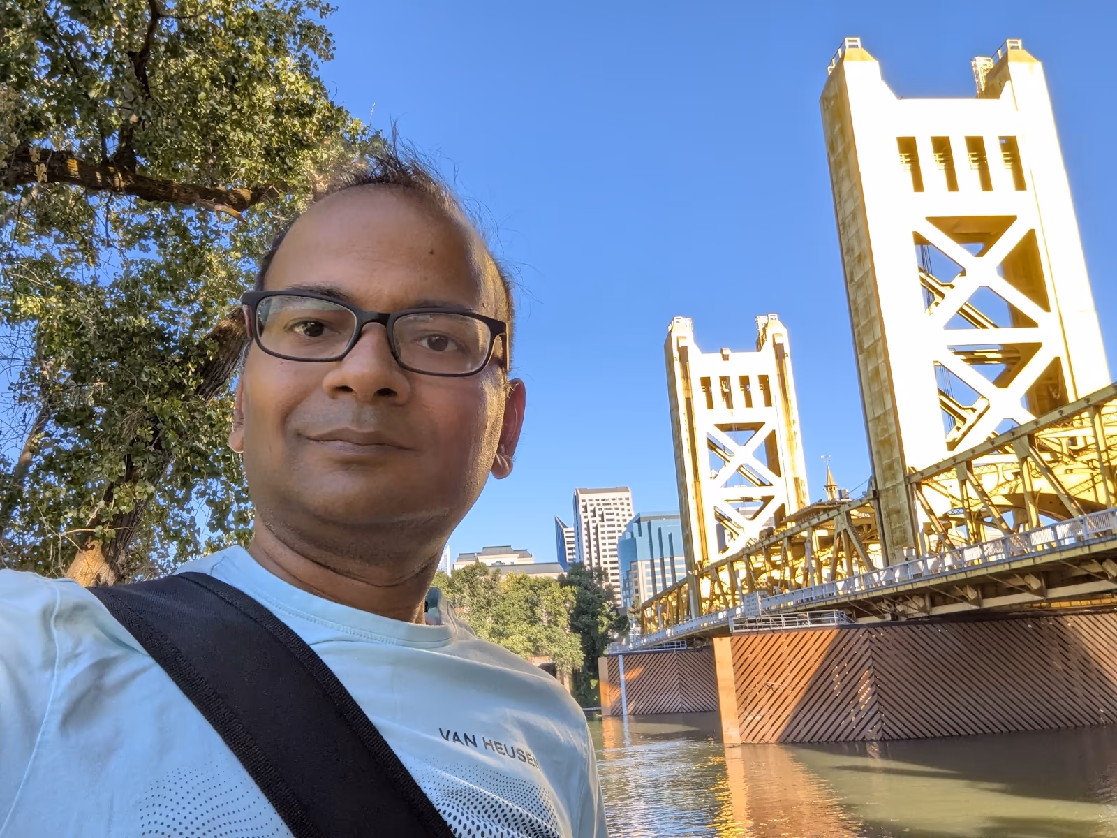 JB in front of Sacramento's Tower Bridge — the golden vertical lift bridge rising behind him, clear blue California sky above, the Sacramento River below