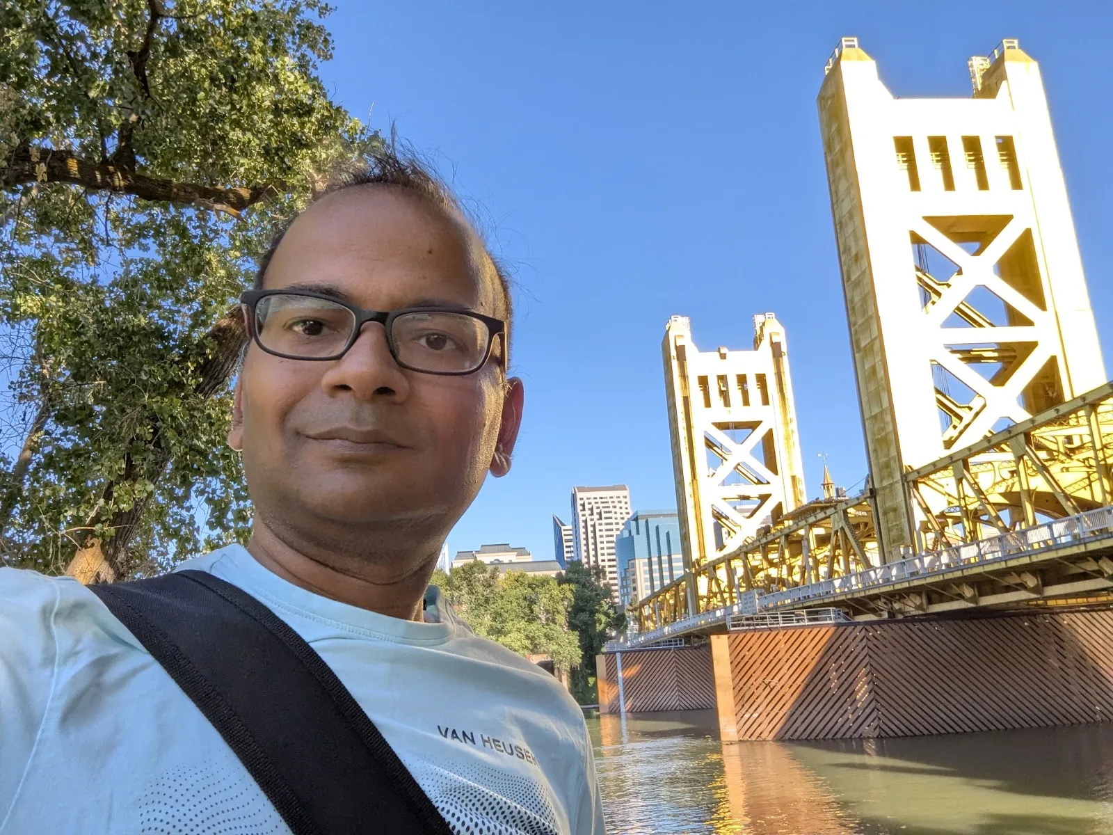 JB in front of Sacramento's Tower Bridge — the golden vertical lift bridge rising behind him, clear blue California sky above, the Sacramento River below